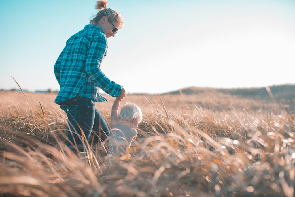 Mother holding toddler's hand walking through field of long grass
