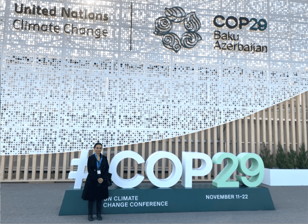 Dr. Mili Roy stands in front of a "#COP29" sign at the UN Climate Change Conference in Baku, Azerbaijan