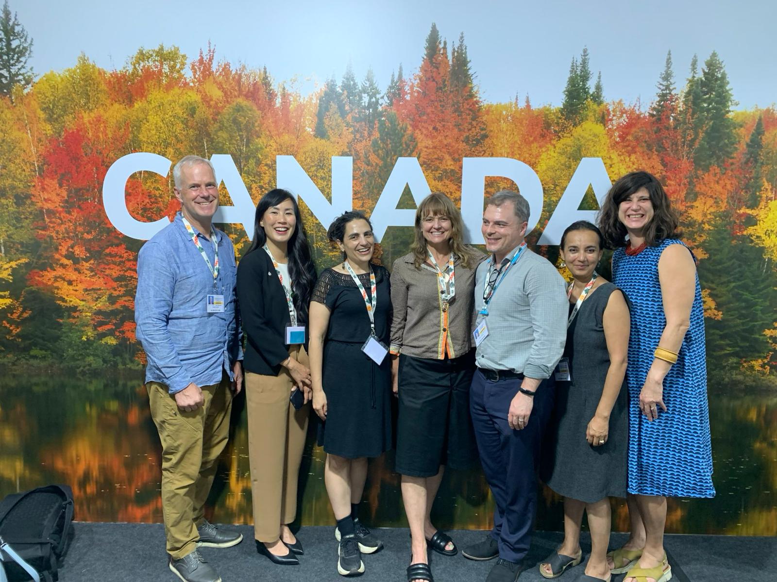 The CAPE team poses in front of a printed Canada backdrop of an autumn forest at COP30